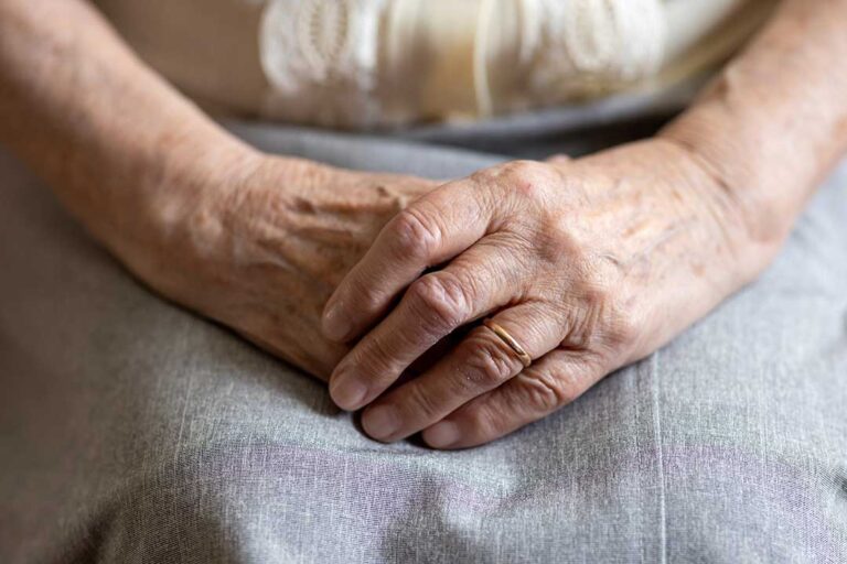 An older adult reviews a medication organizer with a family member in a bright home setting.